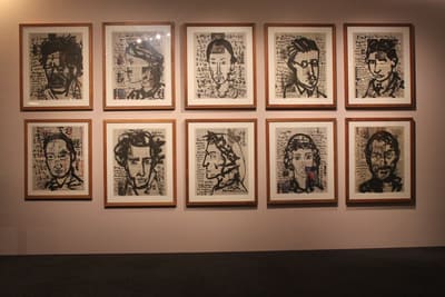A photo of an exhibition wall. Ten ink portraits on newspapers are framed up and hung on the wall.