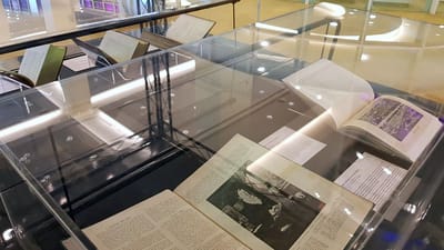 Photo of the showcases, with books inside. They are opened up, and the book closest to the foreground has an image of Sir Stamford Raffles. The book next to it has a photograph of a crowd.