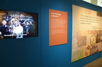 A close-up of the Arts Heritage introduction wall. A TV is showing a video with a concert performance.