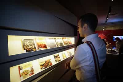 Brightly lit shelves with cookbooks are on display, with a visitor looking at them.
