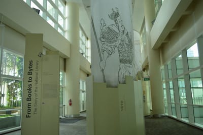 Photo of the front entrance of the From Books to Bytes gallery. A tall cloth banner hangs over the exhibition, with random book illustrations printed on it.