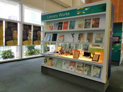 A bookshelf titled: 'Literary Works'. Book cover replicas line the top shelves. In the middle, a lighted showcase feature awards for display.