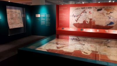 A large image of an old world map is on a red wall. Large showcases are next to it.