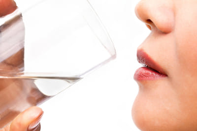 A close-up photo of a woman drinking a glass of water.