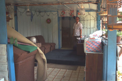 A man stands among some furniture in the living room of his house in Kampong Wak Selat.