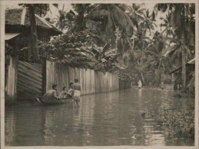 Three individuals share a boat during a flood in a kampong at Geylang Serai, while some others stand in knee-high water.