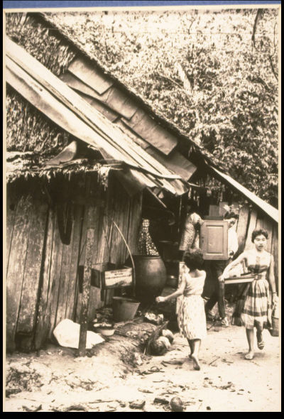 A family carries furniture out of their thatched kampong house.