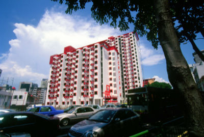 HDB blocks with an orderly red and white facade stand behind some vehicles.