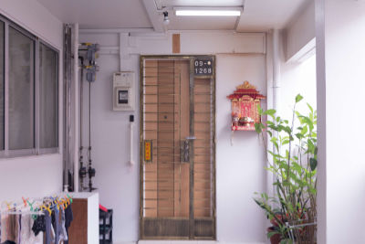 The locked metal gate and wooden door of an HDB flat at the end of a corridor.