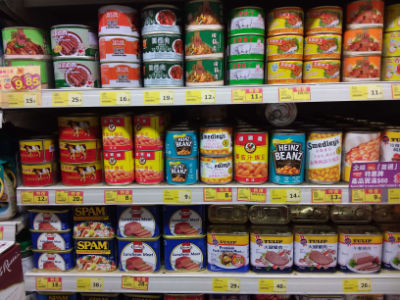 Stacks of canned food items arranged on supermarket shelves with price tags displayed.