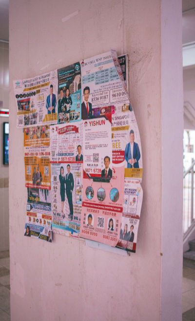 Several printed advertisements of real estate agents overlap on a notice board at a void deck in Yishun.