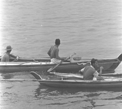 A black and white photo of three men resting seated in their individual sampans during a regatta organised by Ponggol Point Community Centre.