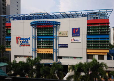 A photograph of Punggol Plaza, a three-story shopping mall in Singapore. The building has a white facade with glass windows and red, blue and yellow trimmings.