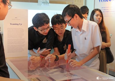 A photo of a tour. Students are looking down into a table showcase.