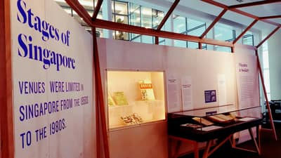 A photo of an exhibition section, titled Stages of Singapore. On the left, there is a table showcase next to a wall.