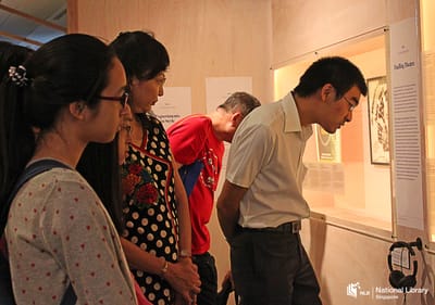 A photo of a tour at the exhibition. Visitors look into a wall showcase.