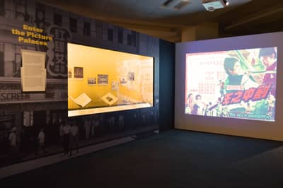 A photo of the Enter the Picture Palaces section. On the left wall, there is a showcase featuring books and images. On the right wall, there is a projection showing classic movie posters.
